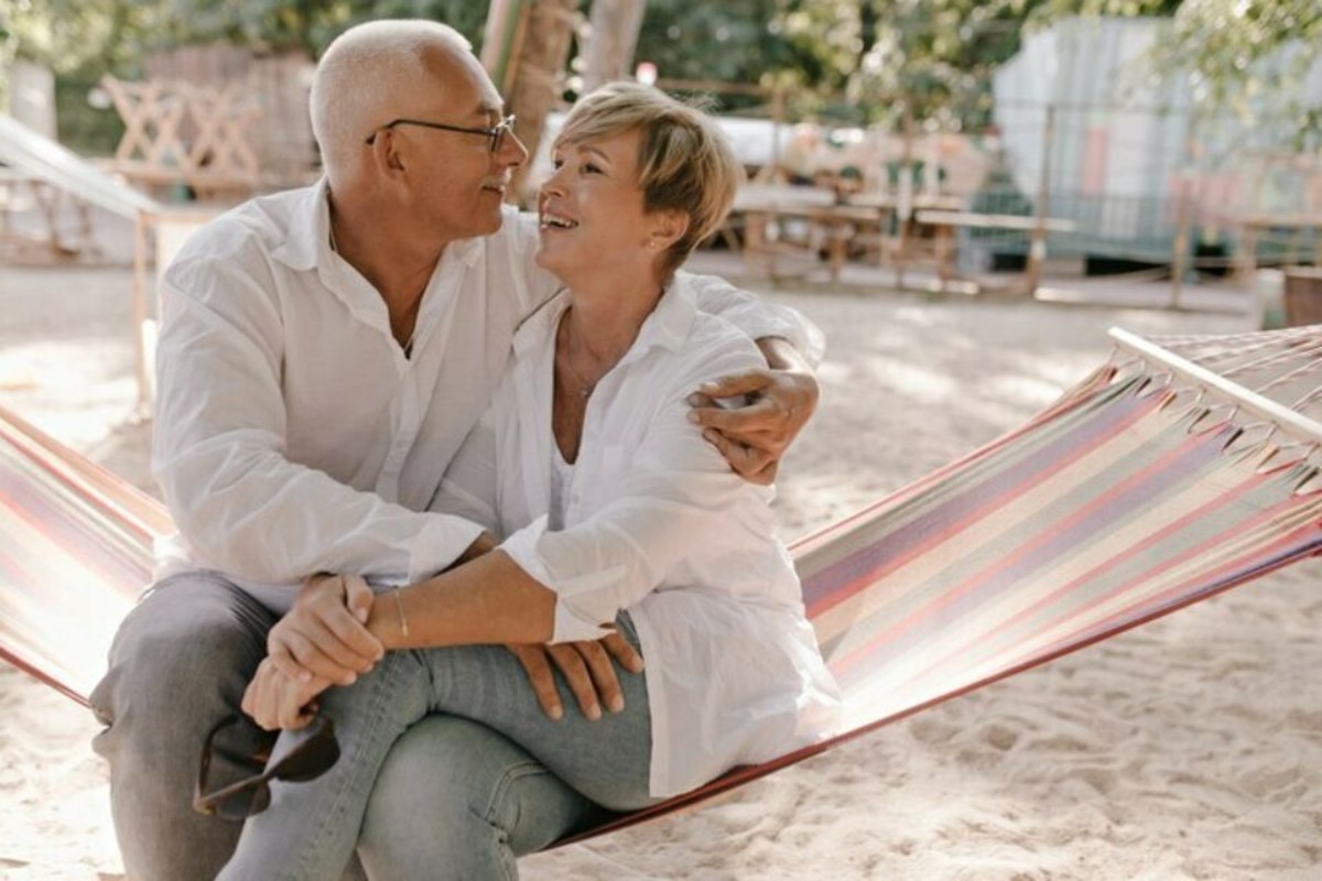 Un couple senior assis dans un hamac coloré, s’enlaçant tendrement et souriant, pour célébrer leurs 55 ans de mariage lors des noces d’orchidée, symbole d’amour durable et raffiné.
